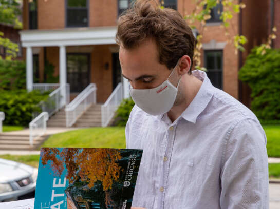 Student in mask, reading The Gate magazine outside.